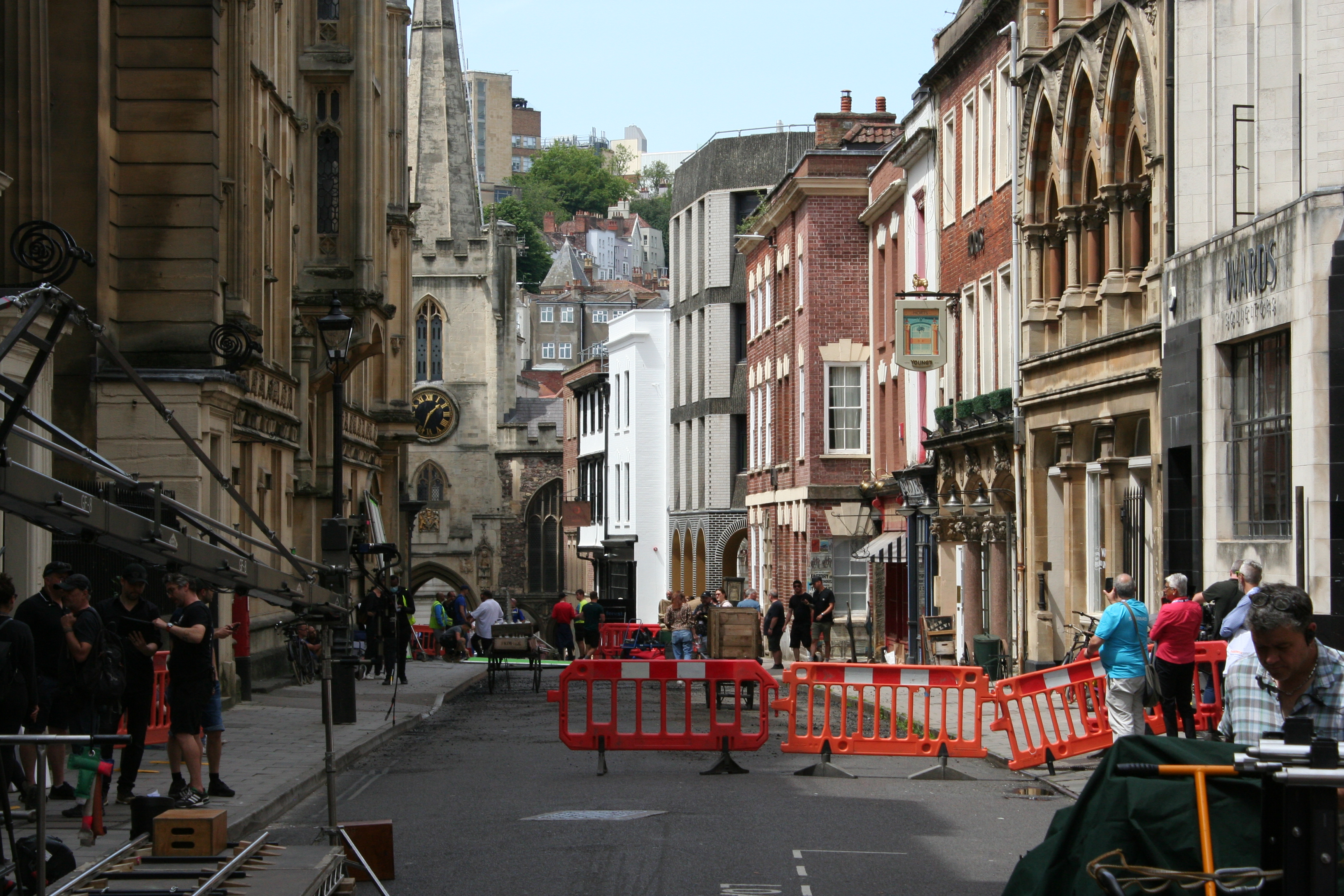 A street closed with orange barriers, camera equipment on track, and a crew in black along the pavement.