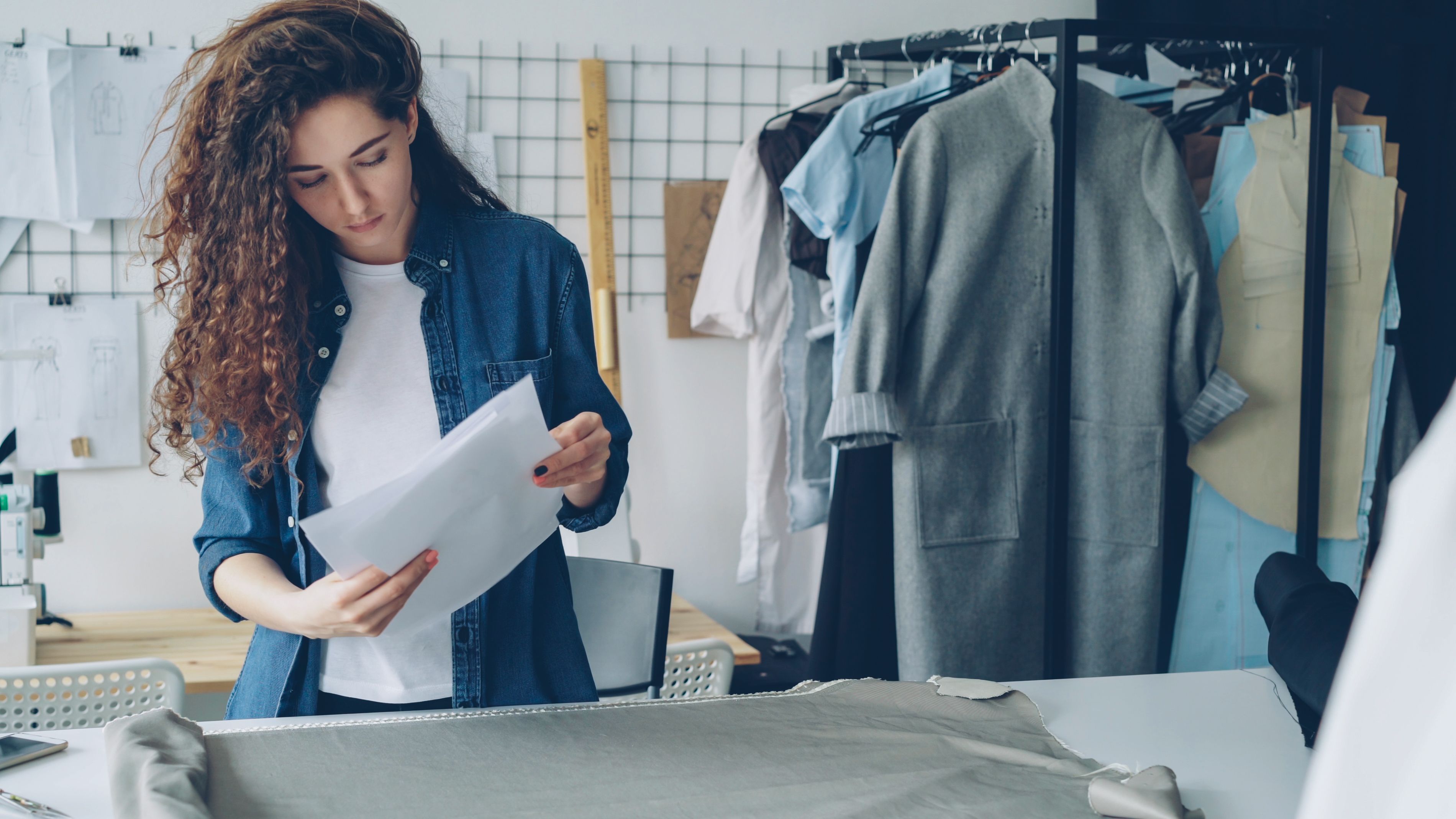 Fashion designer reviewing garment sketches at a production desk.