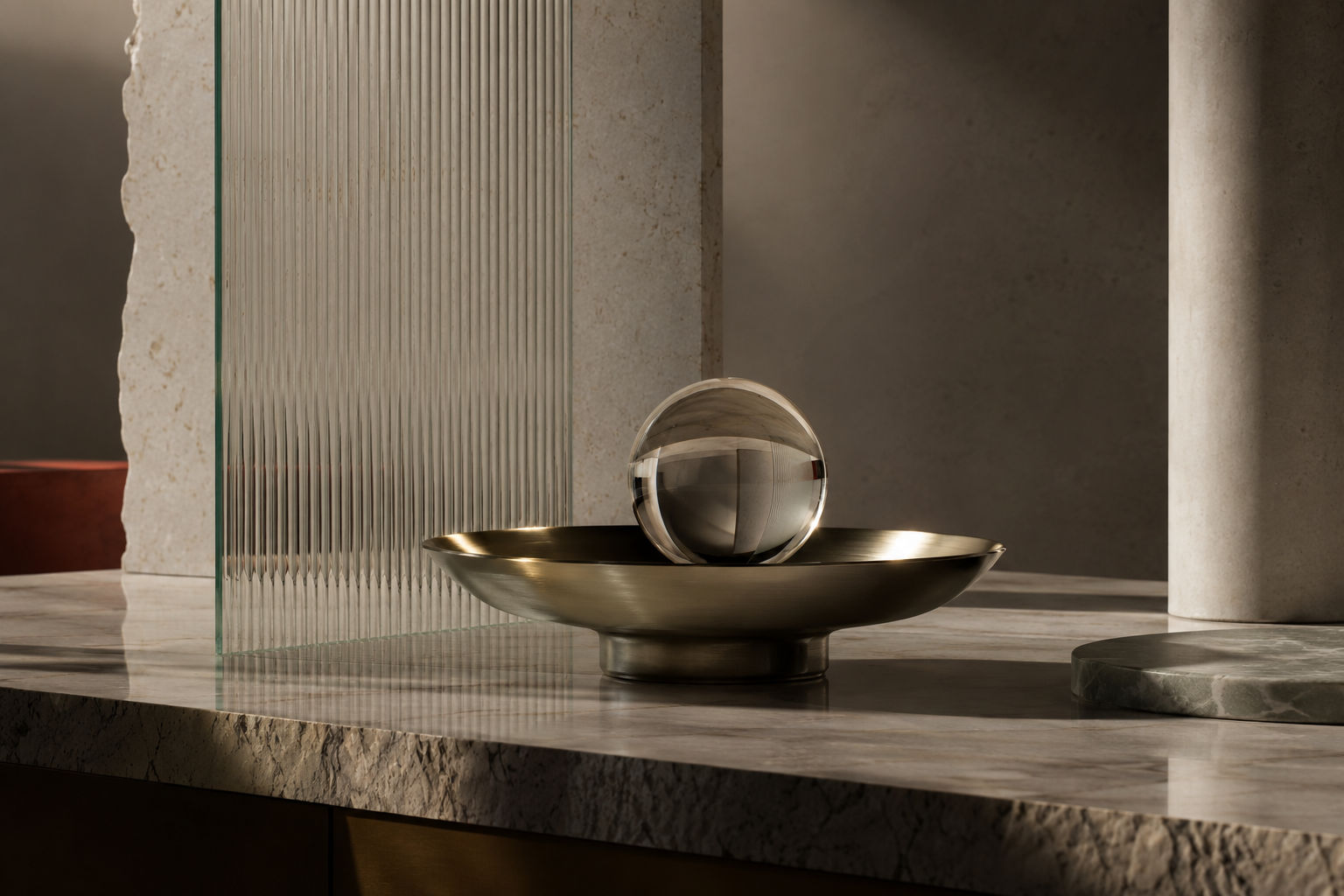 A glass sphere in a brass dish on marble beside fluted glass: matte and polished surfaces in one frame.