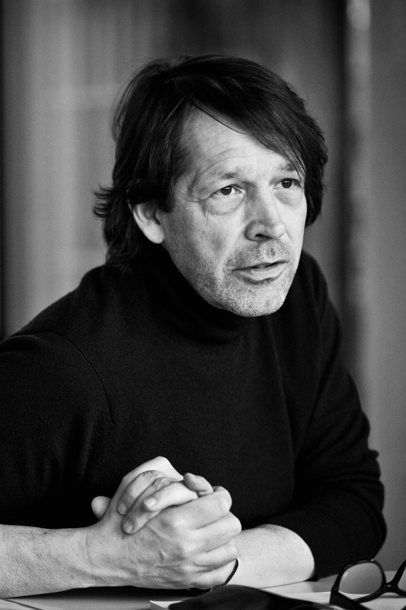 Black-and-white portrait of Peter Saville in a dark turtleneck seated at a table
